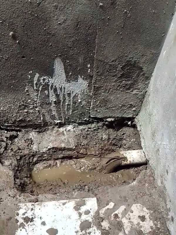 Tubulação de esgoto exposta junto ao muro, com a água voltando a correr após a desobstrução