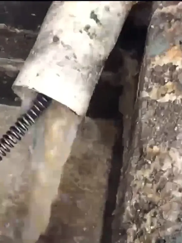 Cabo espiral da máquina desentupidora saindo de um cano de PVC com a água voltando a correr